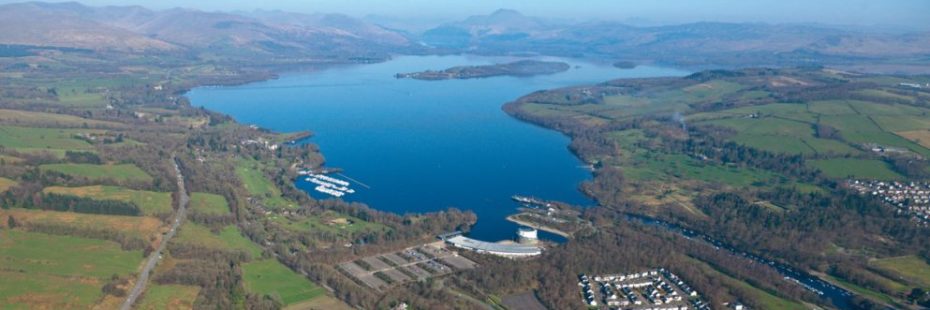 aerial-view-of-balloch-with-loch-lomond-islands-and-ben-lomond-in-the-distance-on-a-blue-skies-day