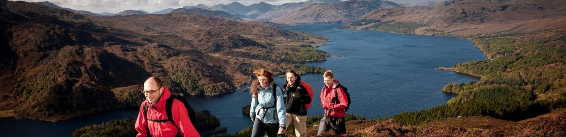 group-of-two-men-and-two-women-climbing-to-the-summit-of-ben-aan-with-loch-katrine-and-trossachs-mountains-in-the-background