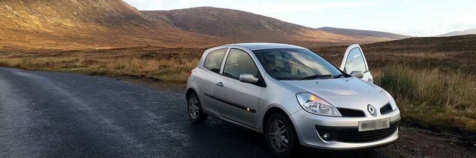 silver-renault-car-parked-on-side-of-the-road-with-brown-hills-behind