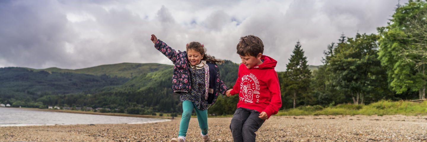 young-girl-and-boy-jump-playfully-in-stream-water-on-ardentinny-beach