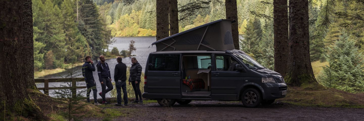 four-friends-hang-around-outside-motorhome-with-stunning-view-of-loch-drunkie-behind