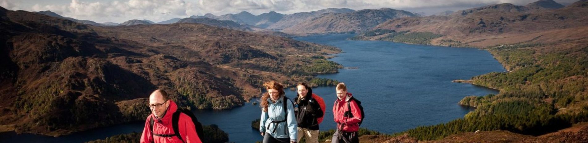 group-of-two-men-and-two-women-climbing-to-the-summit-of-ben-aan-with-loch-katrine-and-trossachs-mountains-in-the-background