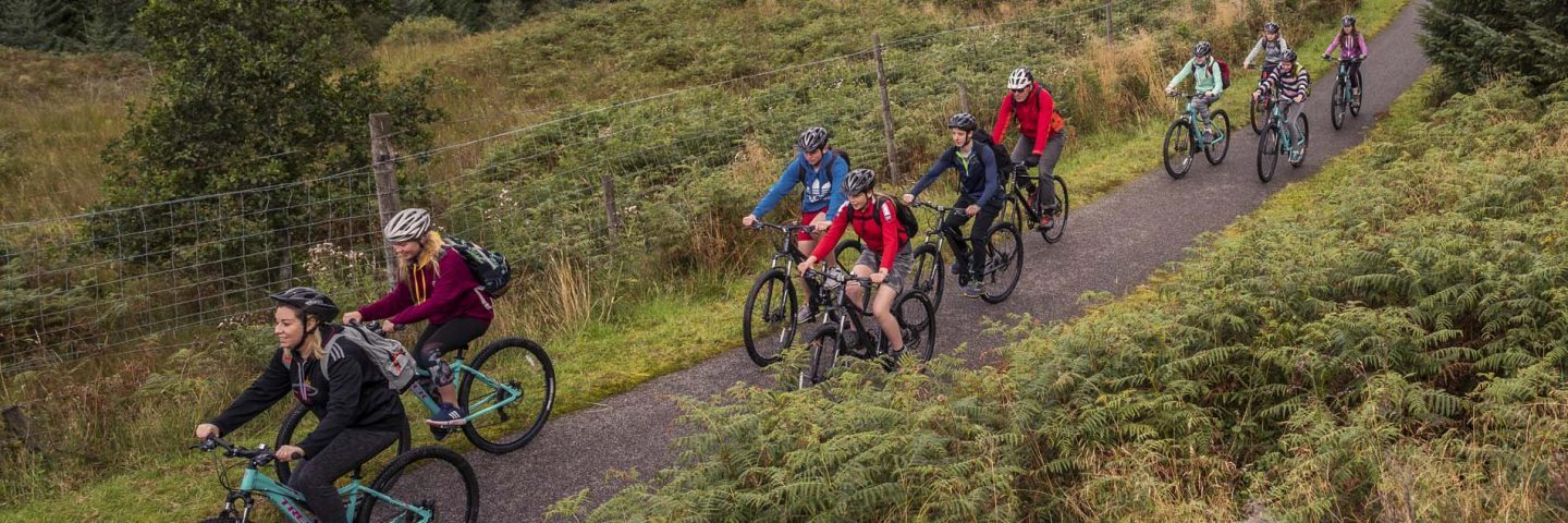 group-of-young-people-in-colourful-clothes-riding-on-bikes-on-national-cycle-route-seven-in-glen-ogle