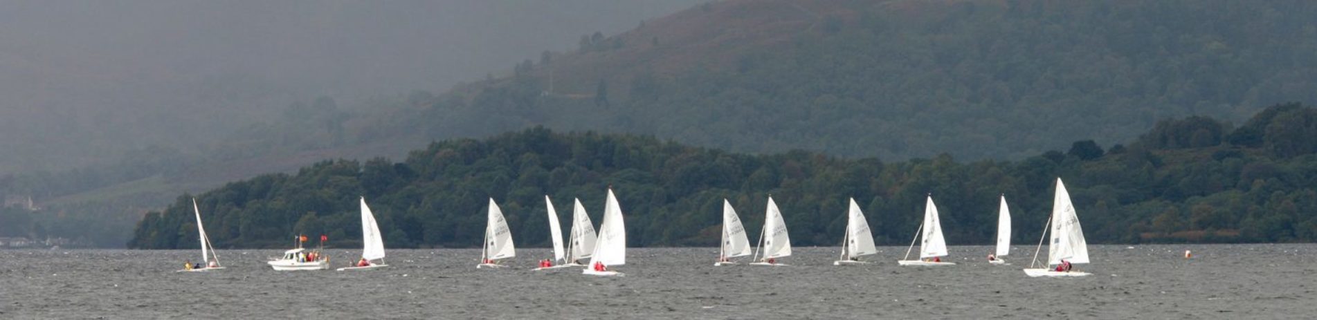 numerous-white-veil-sailing-boats-on-loch-lomond-wooded-shore-behind