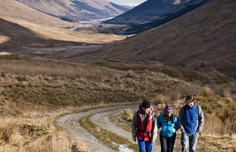 group-of-two-men-and-one-woman-walking-and-chatting-on-glen-track-among-hills