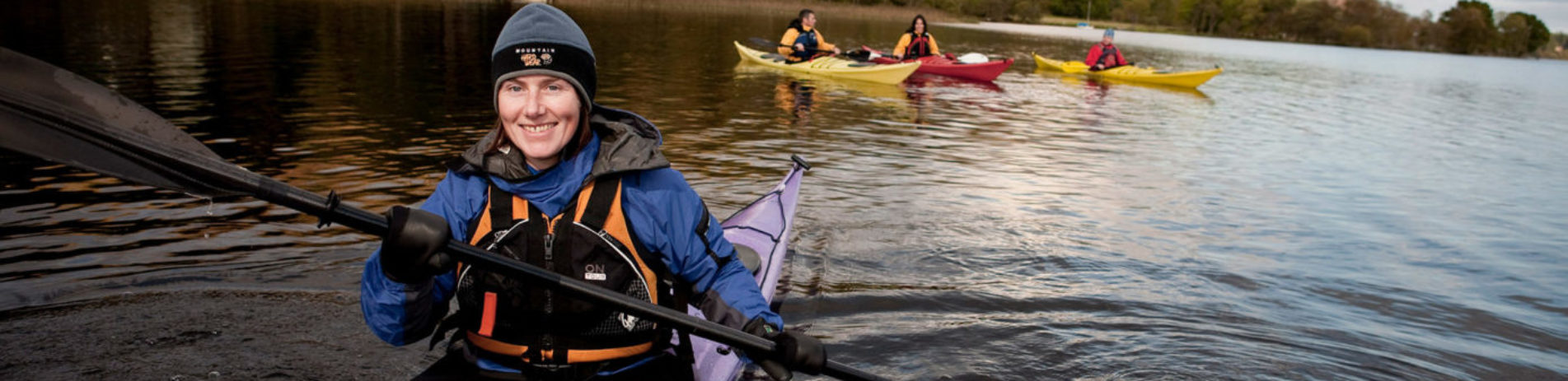 group-of-kayakers-on-loch-with-woman-in-foreground-smiling-while-peddling