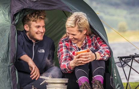 blond-couple-smiling-and-enjoying-a-cuppa-at-tent-entrance-at-edge-of-loch-chon