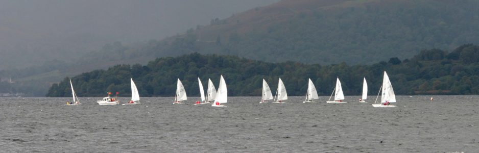 several-sailing-boats-with-white-veils-in-the-distance-on-loch-and-surrounding-high-hills-covered-by-forests-on-the-right