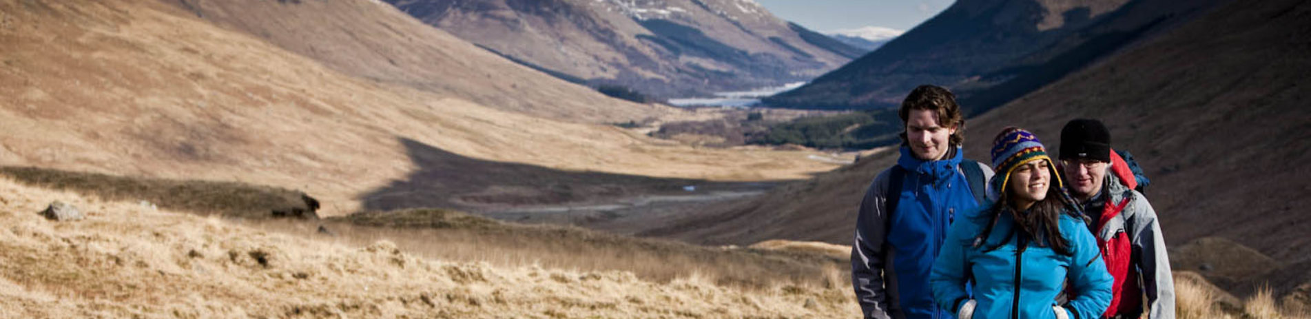 group-of-two-men-and-one-woman-walking-and-chatting-on-glen-track-among-hills