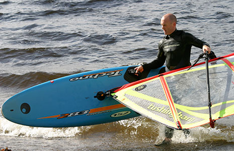 middle-aged-man-in-wetsuit-holding-paddleboard-and-veil-coming-out-of-loch-water
