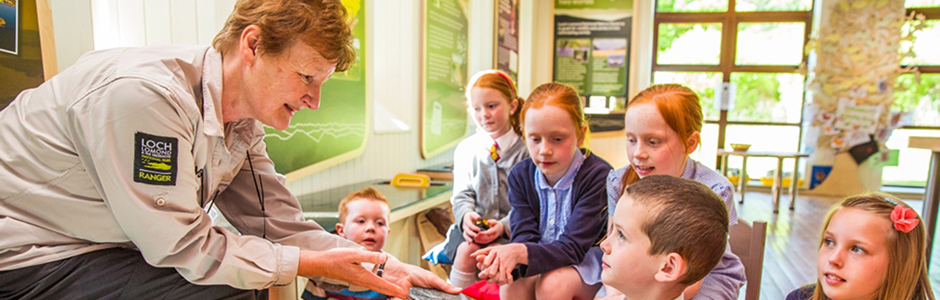 older-ranger-woman-chatting-to-group-of-young-children-in-balmaha-visitor-centre