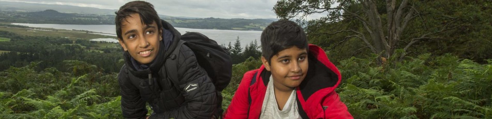 two-young-boys-smiling-surrounded-by-bracken-loch-lomond-visible-in-the-distance