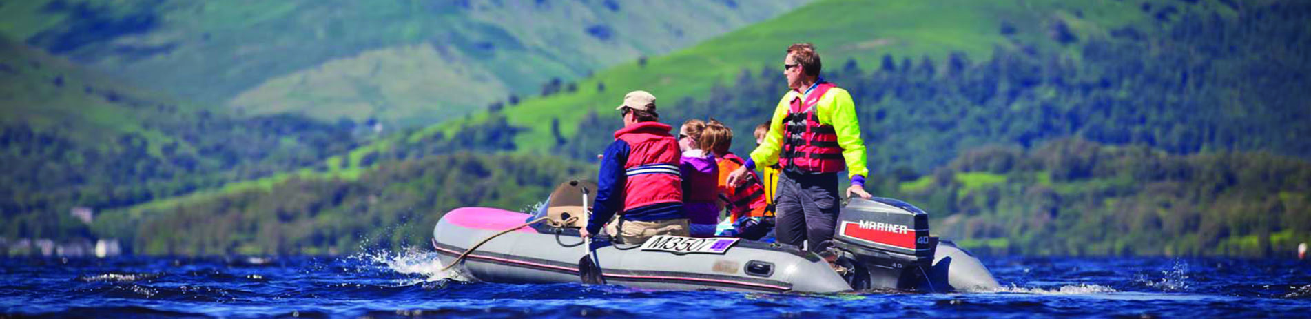 group-of-five-people-in-life-vests-on-motor-boat-on-loch-lomond-with-wooded-shores-in-the-distance