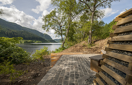 faerie-hollow-scenic-art-installation-platform-of-stone-and-wood-at-edge-of-loch-lubnaig-with-stunning-views-over-forested-shores-and-hills-behind