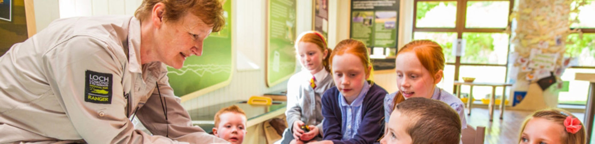 older-ranger-woman-chatting-to-group-of-young-children-in-balmaha-visitor-centre