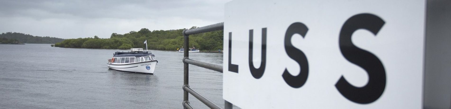 luss-pier-with-luss-name-sign-on-metal-bars-waterbus-on-loch-lomond-approaching-shore