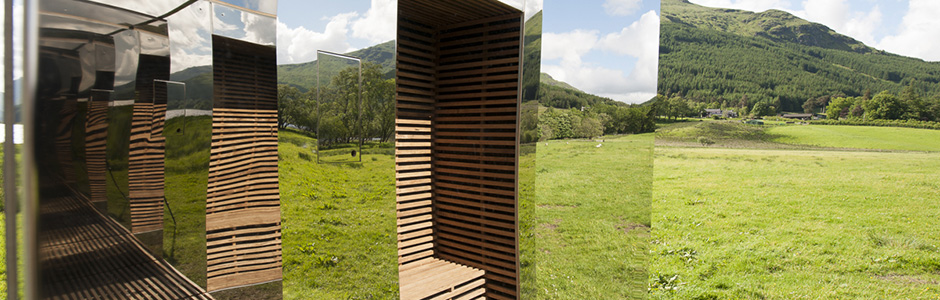 lookout-mirrored-cabin-scenic-art-installation-surrounded-by-green-grass-and-wooded-hills-in-the-distance