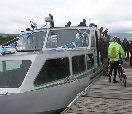 people-disembarking-from-boat-on-pier-one-of-them-is-in-green-waterproof-jacket-next-to-bike