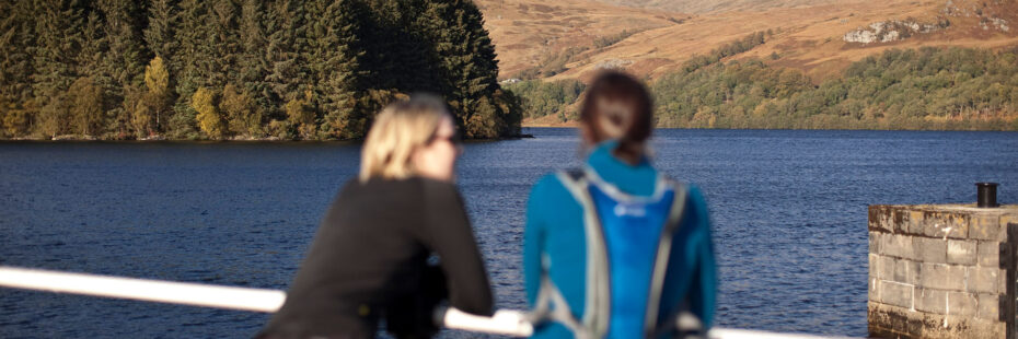 blurred-figures-of-two-women-at-edge-of-pier-looking-into-distance-over-loch-and-surrounding-hills