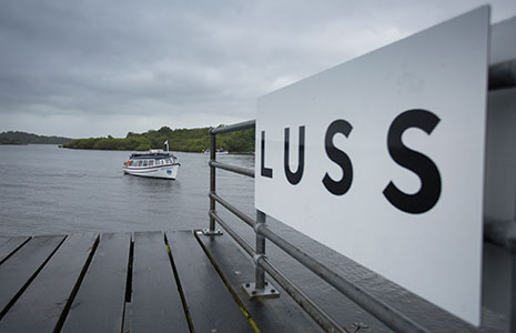luss-pier-with-luss-name-in-close-up-letetrs-on-white-board-with-a-waterbus-on-loch-lomond-behind-approaching-the-pier