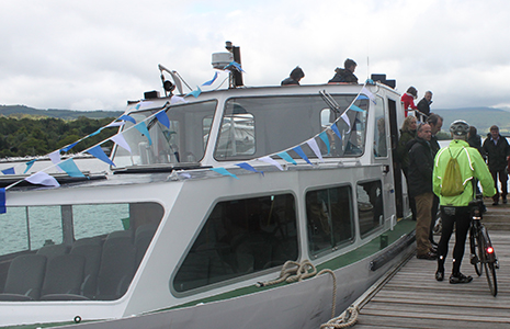 people-disembarking-from-boat-on-pier-one-of-them-is-in-green-waterproof-jacket-next-to-bike