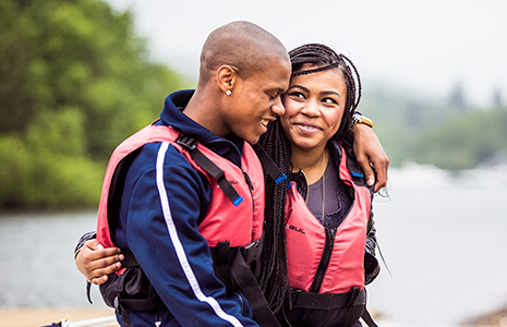 young-couple-wearing-life-vests-on-edge-of-loch-looking-wat-each-other-affectionately