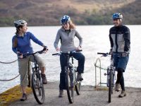 three-cyclists-two-women-one-main-with-bikes-and-helmets-on-edge-of-pier-loch-behind-them