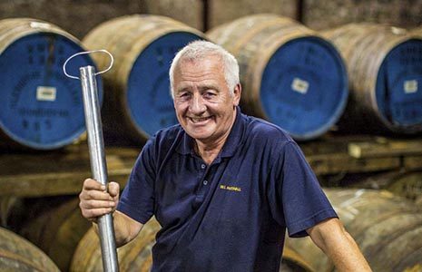 man-in-blue-t-shirt-and-short-white-hair-smiling-at-camera-in-whisky-distillery