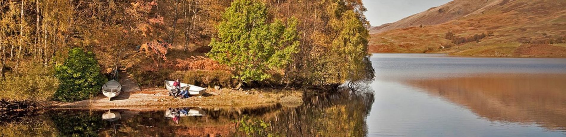 glen-finglas-reservoir-autumn-colours-wooded-shore-two-boats-moored-on-left-with-couple-of-people-resting-next-to-them