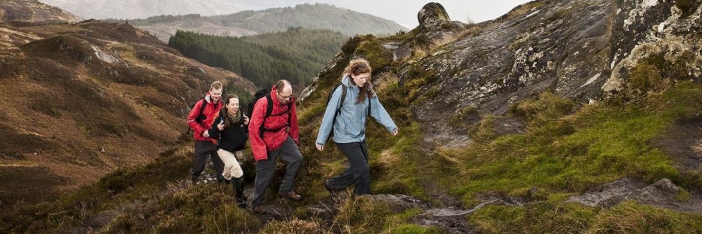 two-men-and-two-women-hiking-up-trail-on-conic-hill-they-are-dressed-in-colourful-outdoor-gear