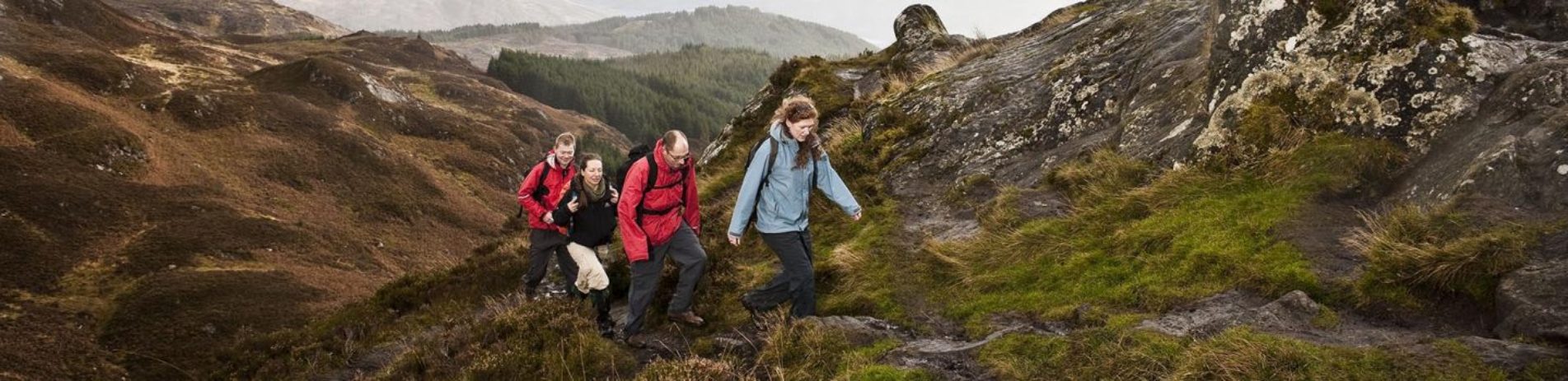 two-men-and-two-women-hiking-up-trail-on-conic-hill-they-are-dressed-in-colourful-outdoor-gear