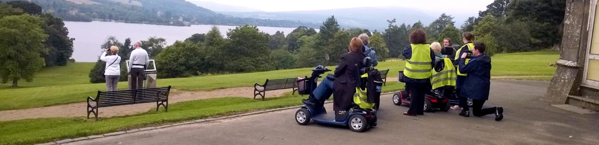 mobility-scooter-drivers-accompanied-by-people-in-high-viz-jackets-looking-into-distance-to-loch-lomond-from-balloch-castle