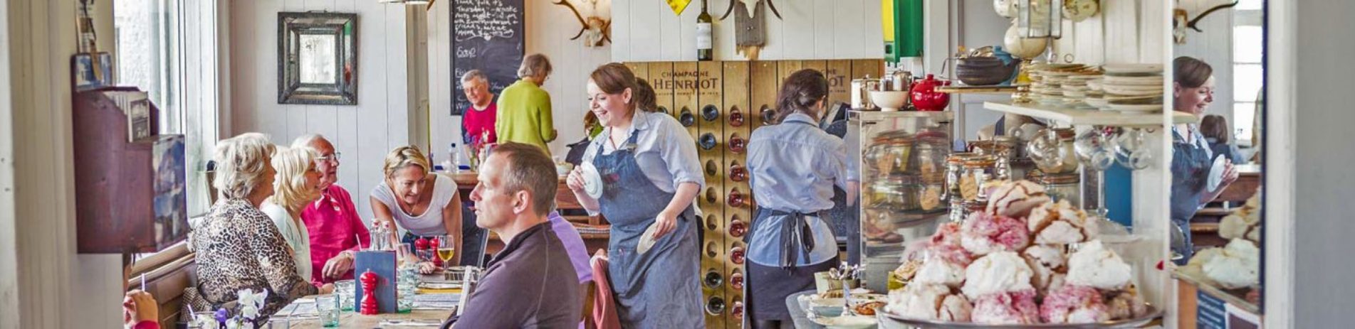 mhor-eighty-four-restaurant-interior-meringues-visible-on-plate-on-right-and-smiling-waitress-attending-to-table-of-men-and-women-on-left-everything-is-very-colourful