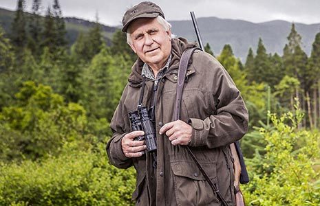 stalker-older-man-holding-gun-strap-and-binocular-at-edge-of-forest