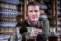 man-with-short-curly-brown-hair-in-sweater-holding-whisky-glass-in-distillery-room