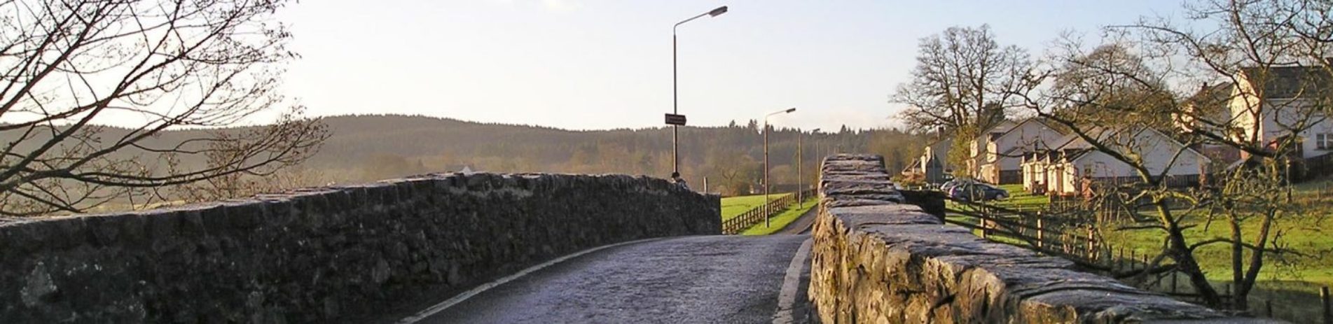 old-arched-bridge-with-farmland-and-houses-in-the-distance-in-sunshine