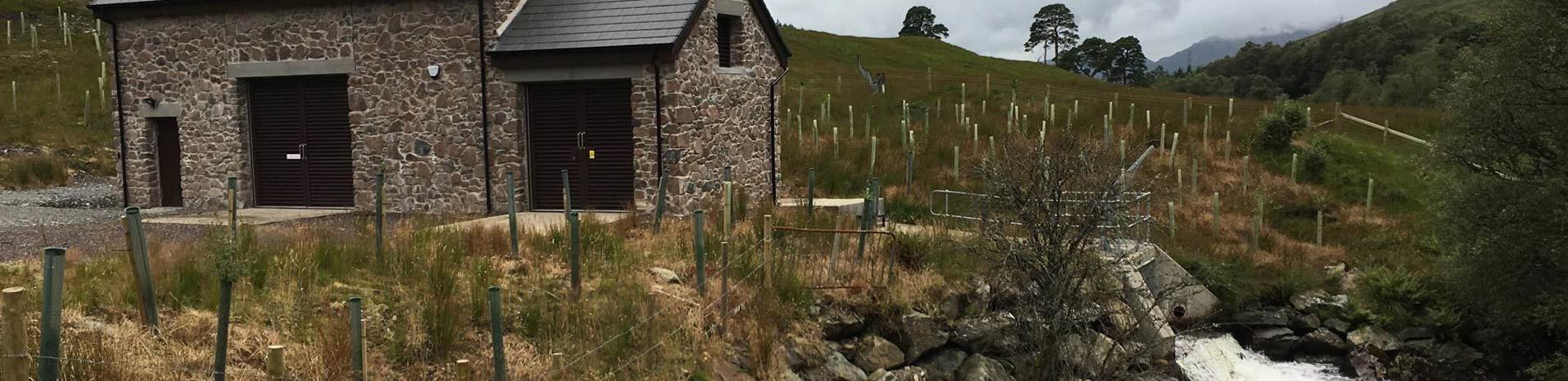 run-of-river-hydro-scheme-beautiful-stone-building-with-sleet-roof-next-to-stream-and-hillside-with-dozens-of-newly-planted-trees-in-tree-guards