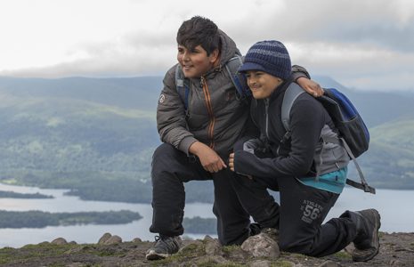 two-young-boys-on-rock-looking-into-distane-loch-lomiond-and-island-visible-behind-them