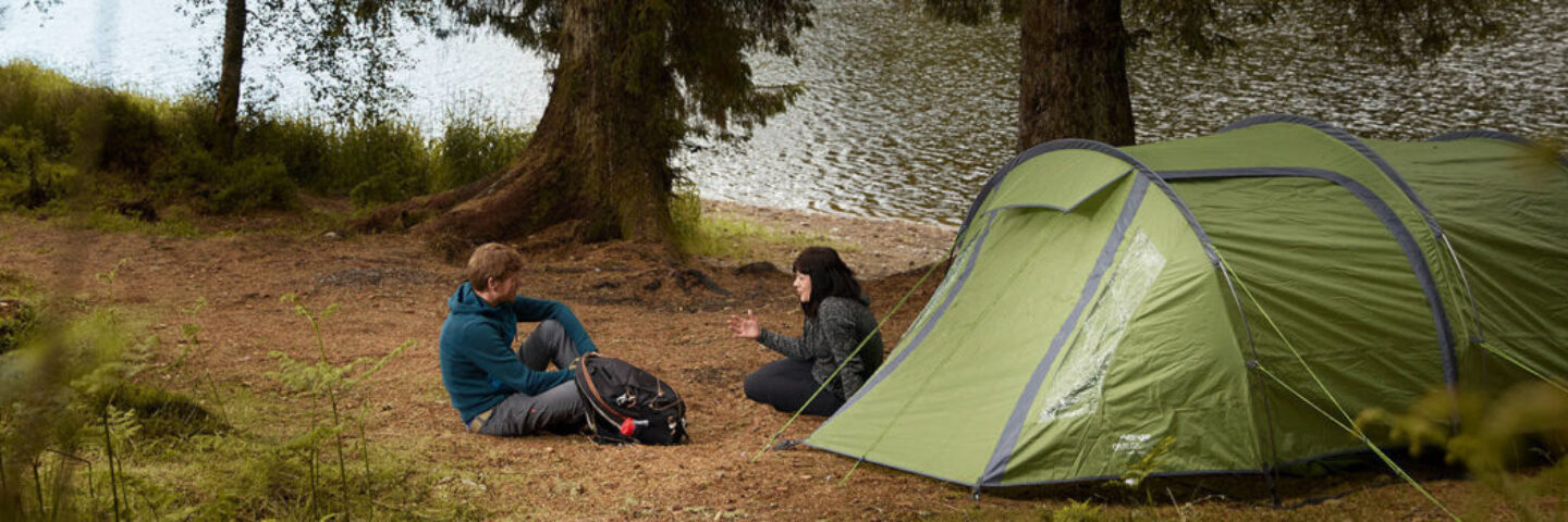 blonde-woman-holding-baby-at-blue-tent-entrance-at-edge-of-loch-chon