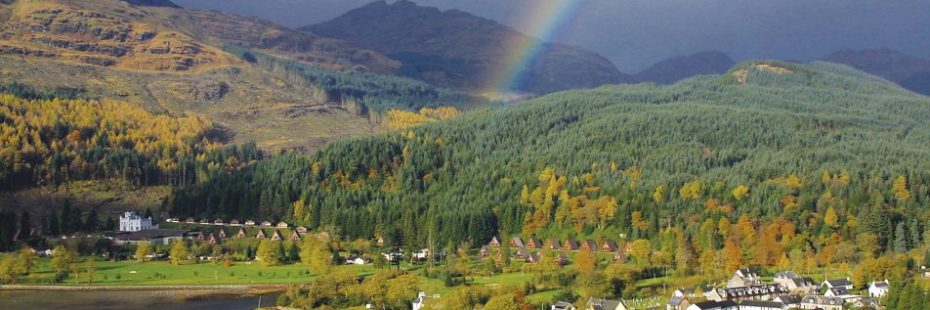 rainbow-over-village-with-forest-covered-hillside-and-mountains