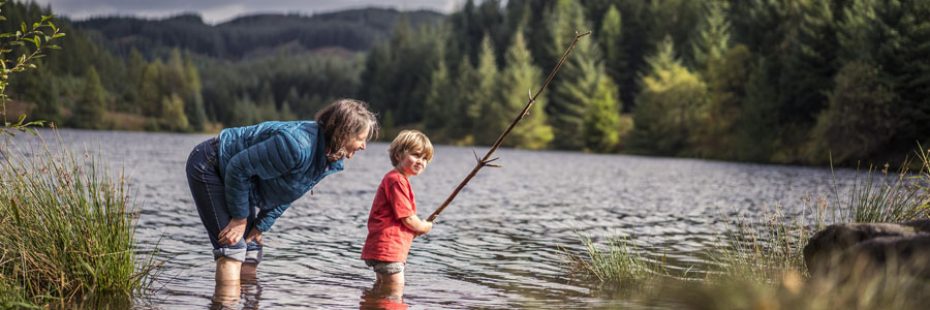 woman-and-young-boy-submerged-in-water-to-their-kneww-in-loch-drunkie-boy-is-holding-long-stick-mock-fishing-rod