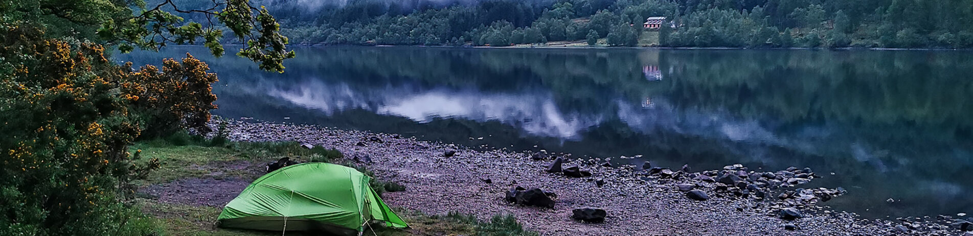 blonde-woman-holding-baby-at-blue-tent-entrance-at-edge-of-loch-chon