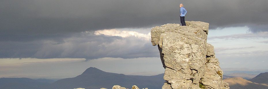 person-stood-on-rock-stack-with-cloudy-mountains
