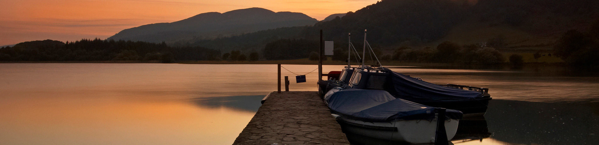 ferry-pier-at-sunset-at-lake-of-menteith-with-moored-boats-one-end-and-hills-in-the-distance