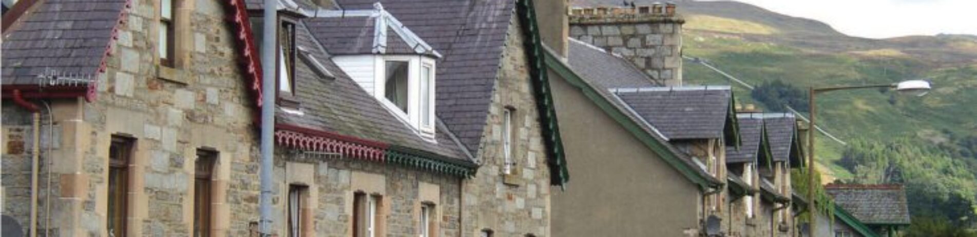 killin-village-main-street-old-stone-victorian-houses-with-colourful-shop-entrances-and-flowers-high-mountains-visible-behind-on-right