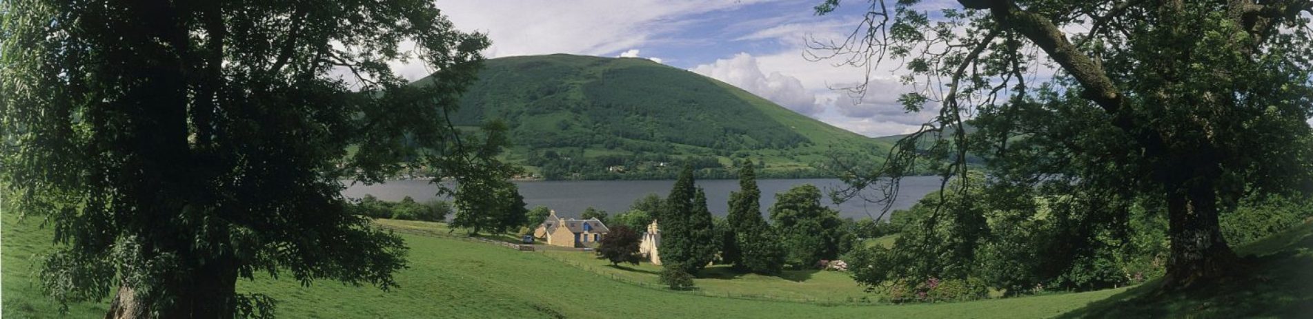 looking-through-trees-across-to-loch-earn-and-lochearnhead-village-forested-hills-in-the-background-blue-skies-with-some-clouds-above