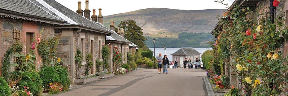 luss-pier-road-loch-lomond-in-distance-tourists-walking-pretty-houses-with-flowers-outside-on-both-sides