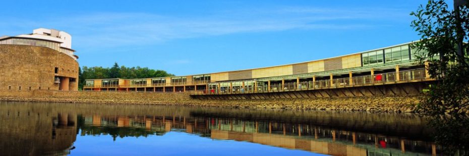 loch-lomond-shores-complex-at-edge-of-loch-lomond-water-in-sunshine-with-trees-behind-on-left