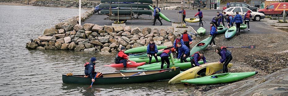 group-of-children-wearing-life-vests-preparing-kayaks-for-launch-at-edge-of-loch-goil-in-lochgoilhead-village