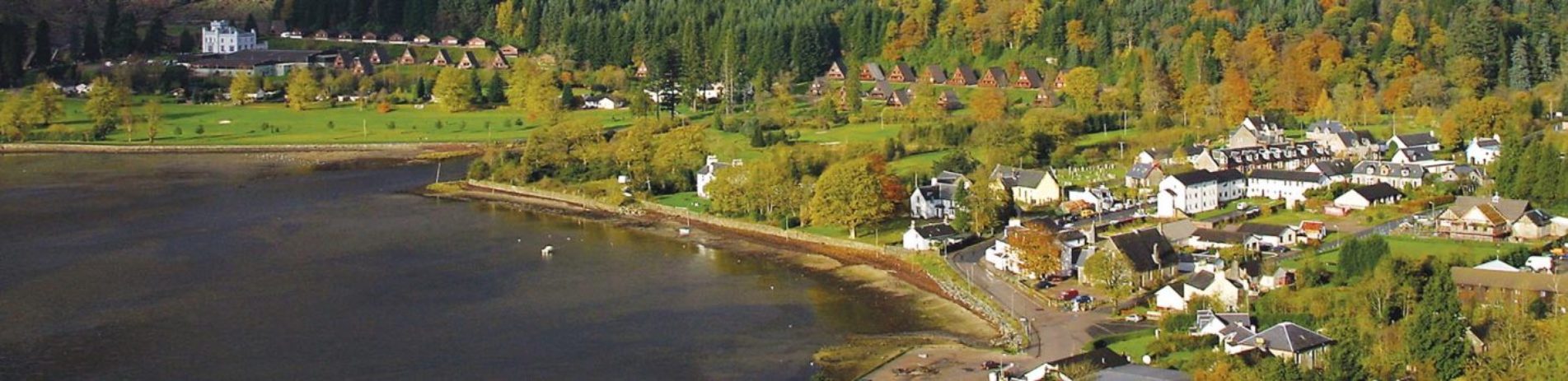lochgoilhead-village-in-sunshine-surrounded-by-greenery-and-holiday-chalets-on-shore-of-loch-goil